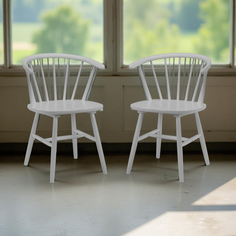 Two white wooden chairs in a room with large windows showing greenery outside.