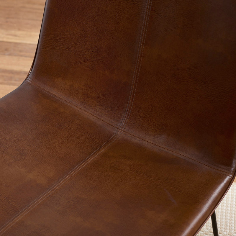 Close-up of a brown leather chair seat with visible stitching on a wooden floor.