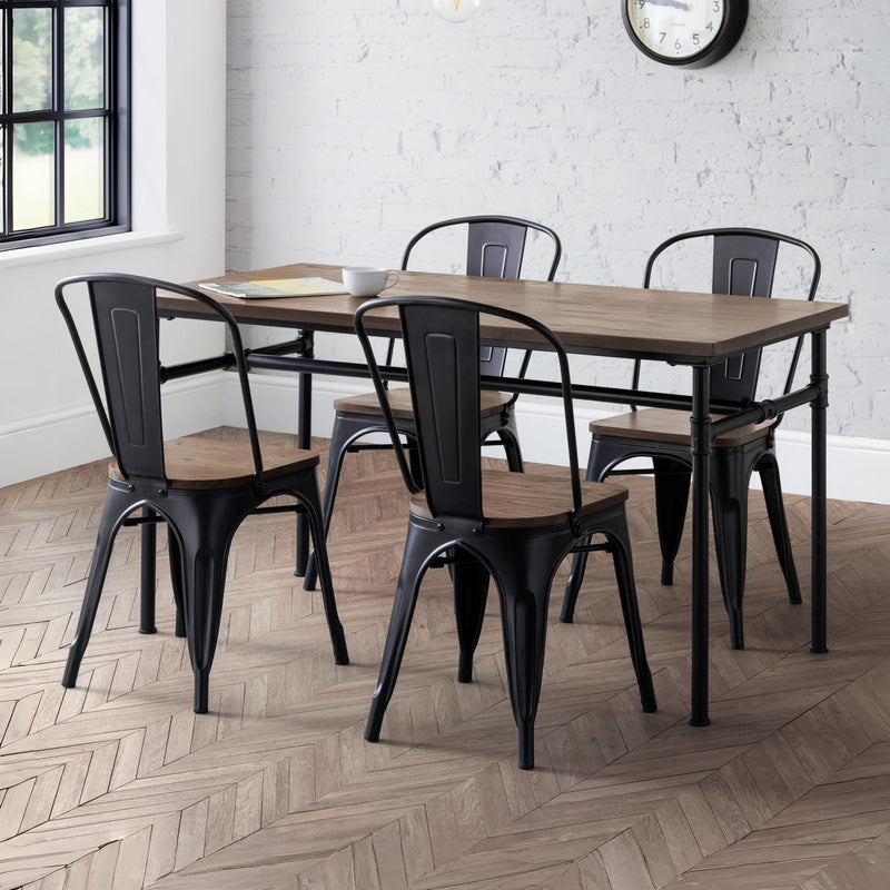 Dining set with wooden table and black metal chairs in a room with white brick walls and a clock.