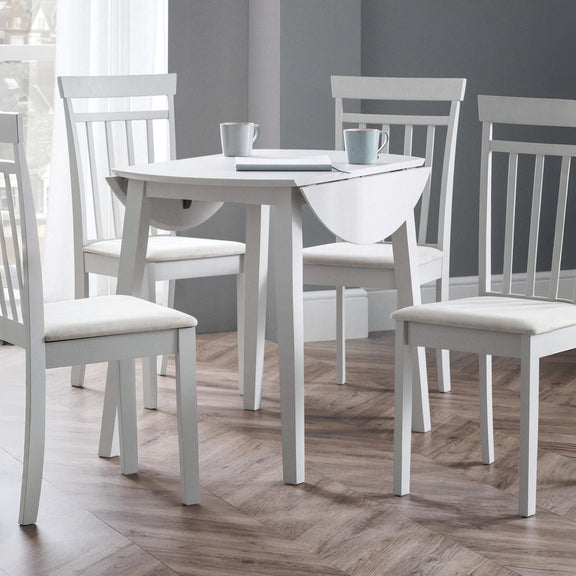 White dining table with four chairs on a wooden floor against a gray wall.