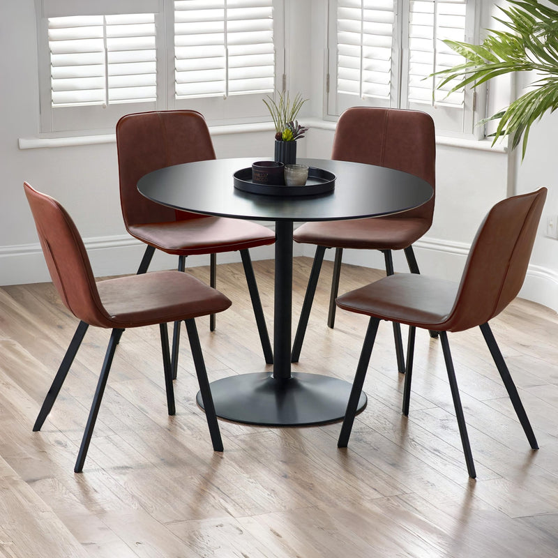 Round black dining table with four brown chairs in a room with light wood flooring and white walls.