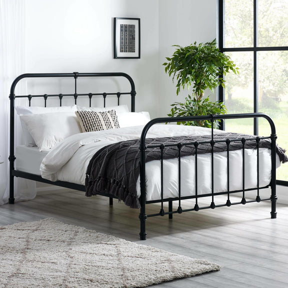 Black metal bed frame with white bedding in a room with a large window and plant.