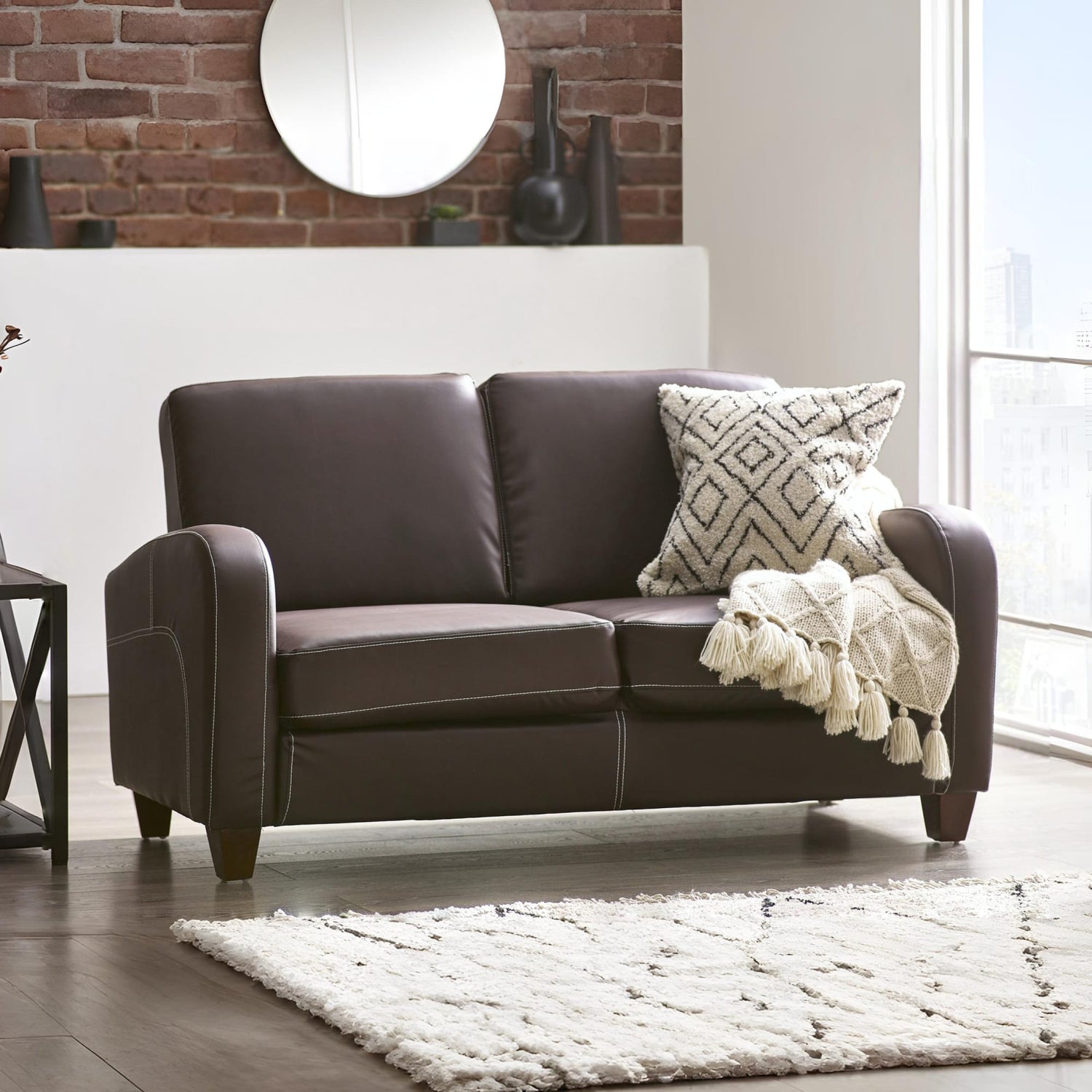 Brown leather sofa with a patterned pillow and blanket in a living room setting.