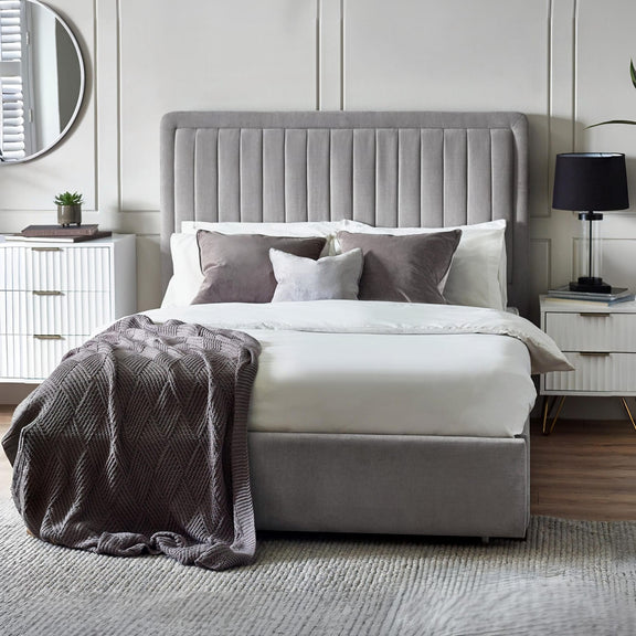 Gray upholstered bed with white bedding and gray throw in a bedroom setting.