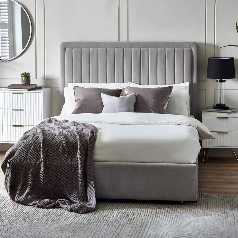 Gray upholstered bed with white bedding and gray throw in a bedroom setting.