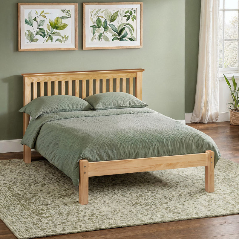 Wooden bed with green bedding in a room with green walls and framed botanical art.