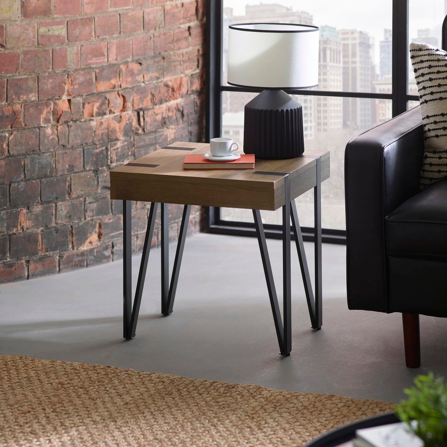 Wooden side table with a lamp and cup against a brick wall in a modern living room.
