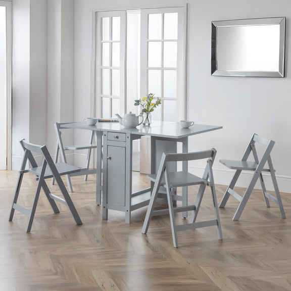 Gray dining table with four matching chairs in a bright room with large windows.