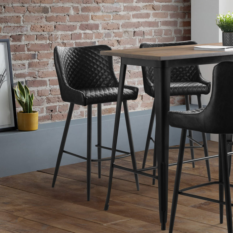 Modern bar stools with a wooden table against a brick wall.