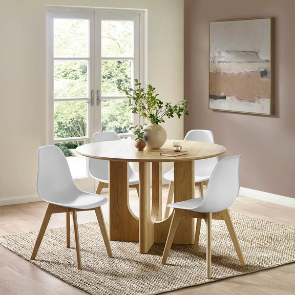 Dining room with a round wooden table and white chairs, featuring a large window and abstract painting.