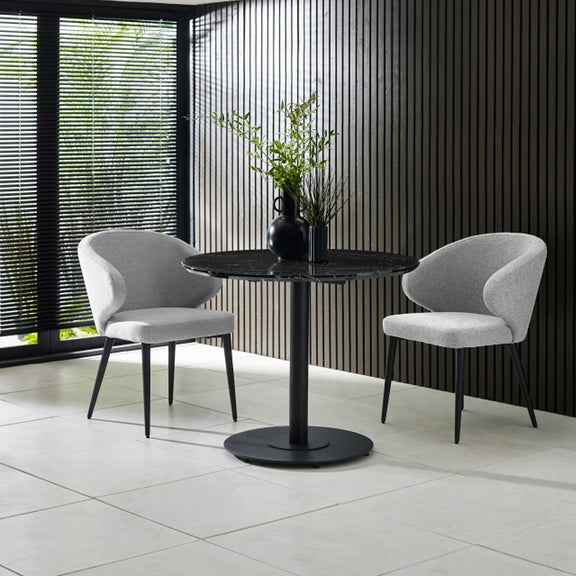 Two gray chairs around a black round table with a plant in a modern interior setting.