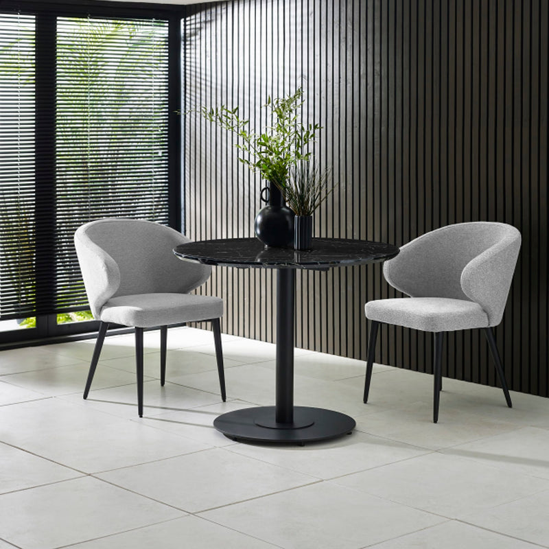 Two gray chairs around a black round table with a plant in a modern interior setting.