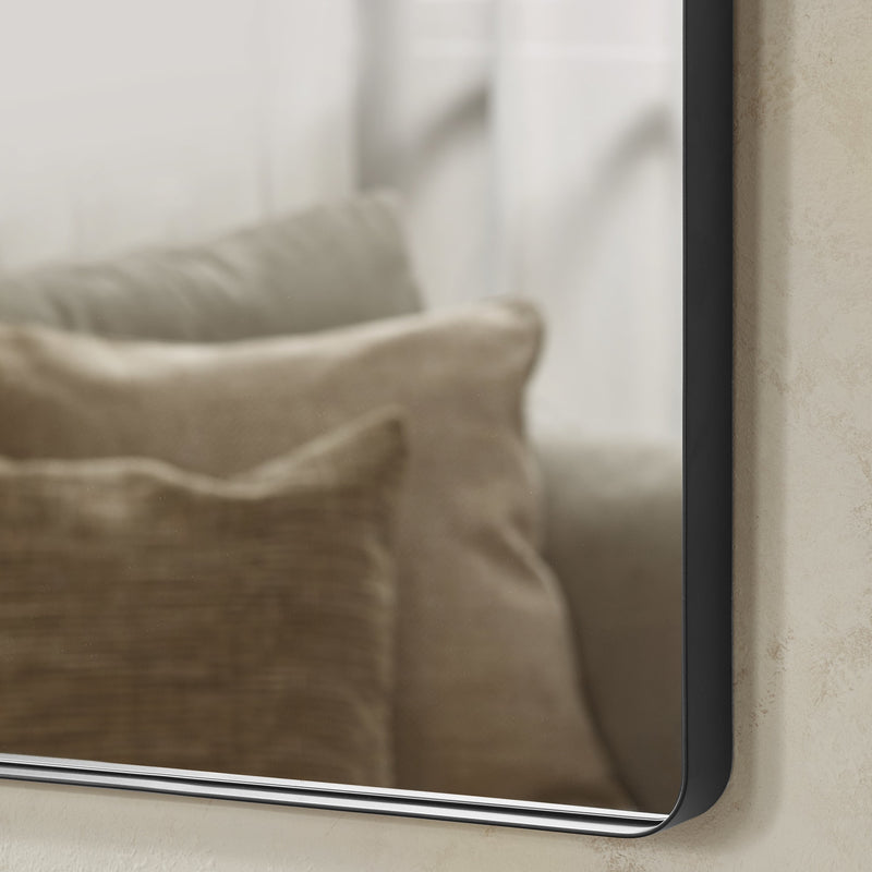 Rectangular mirror with black frame reflecting a beige pillow on a neutral background