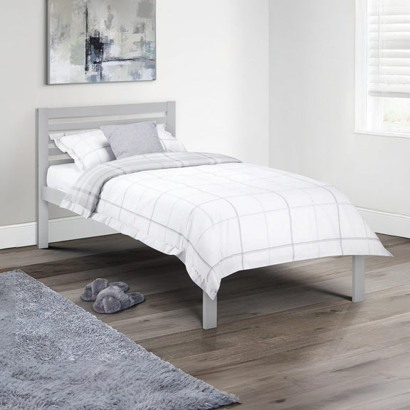 Bedroom with a gray bed frame and white bedding, featuring a gray rug and slippers on a wooden floor.