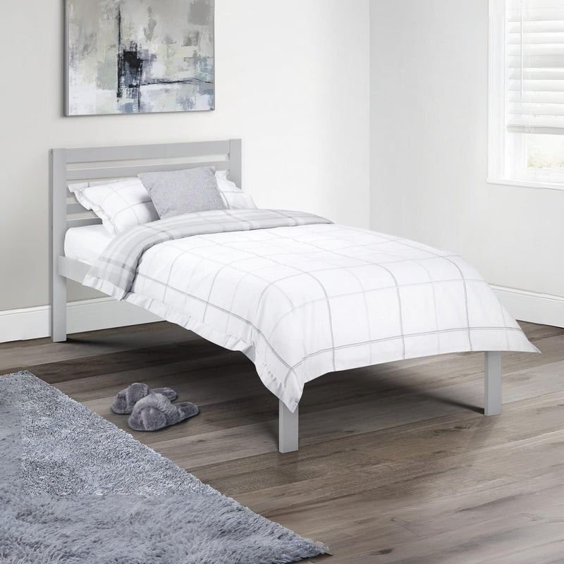Bedroom with a gray bed frame and white bedding, featuring a gray rug and slippers on a wooden floor.