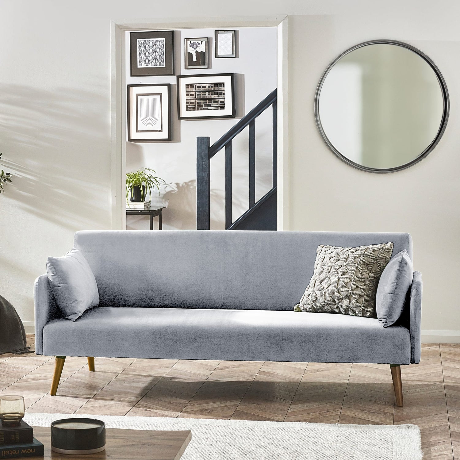 Gray sofa in a living room with a mirror and framed pictures on the wall.