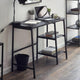 Black desk with laptop, books, and a lamp in a room setting.