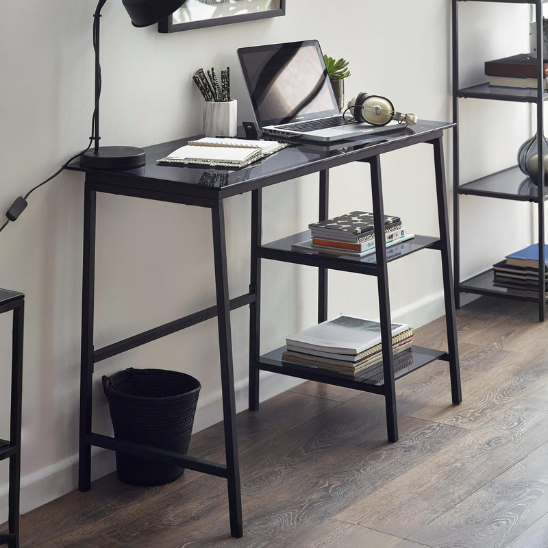 Black desk with laptop, books, and a lamp in a room setting.