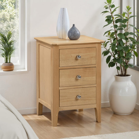 Wooden nightstand with three drawers in a room with plants and a window.