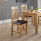 Wooden dining table with two chairs in a room with a gray wall and wooden floor.