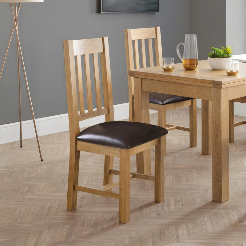 Wooden dining table with two chairs in a room with a gray wall and wooden floor.