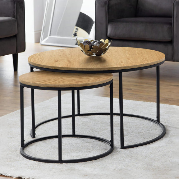 Set of two round wooden coffee tables with black metal bases in a living room setting.