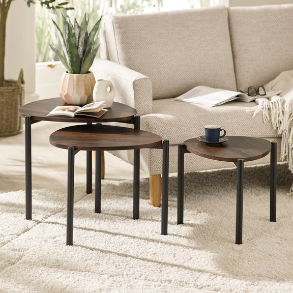 Set of three wooden side tables in a living room setting with a sofa and decor items.