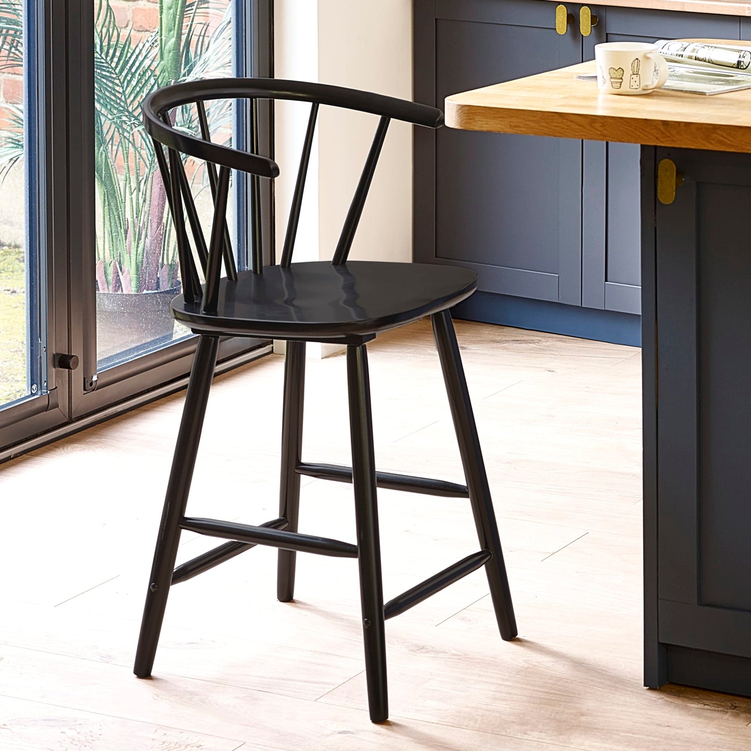 Black bar stool in a kitchen setting with a wooden table and blue cabinets.