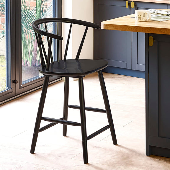 Black bar stool in a kitchen setting with a wooden table and blue cabinets.