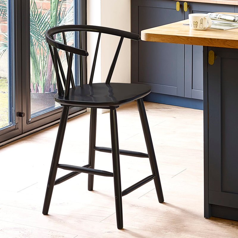Black bar stool in a kitchen setting with a wooden table and blue cabinets.