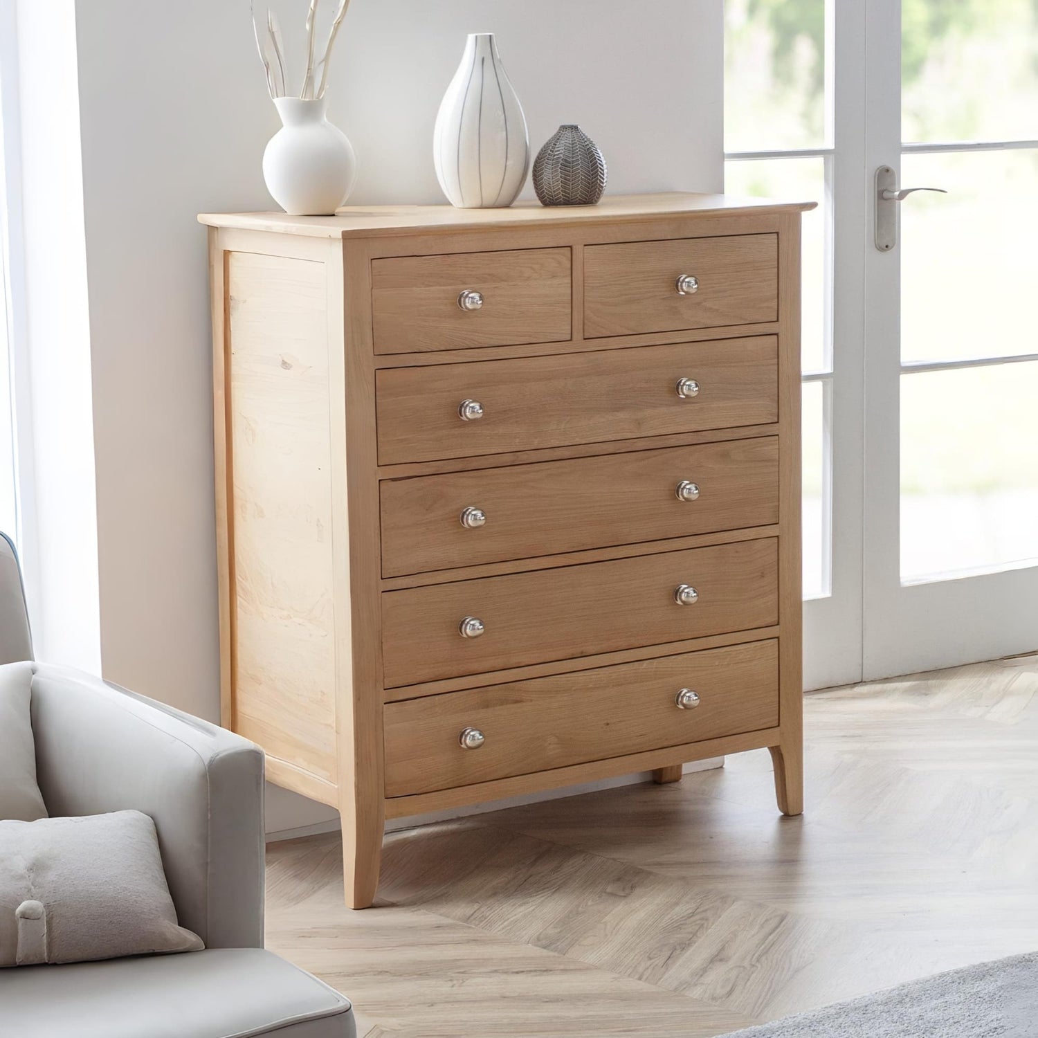Wooden dresser with silver knobs in a room with a light gray sofa and white walls.