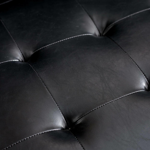 Close-up of a black leather sofa with tufted design
