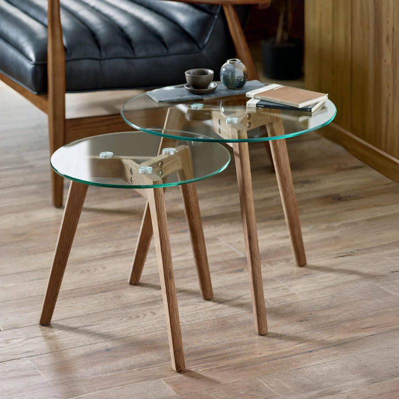 Two glass coffee tables with wooden legs on a wooden floor.