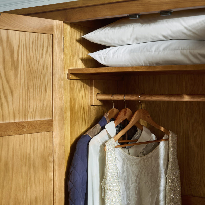 Wooden wardrobe with clothes on hangers and pillows on a shelf