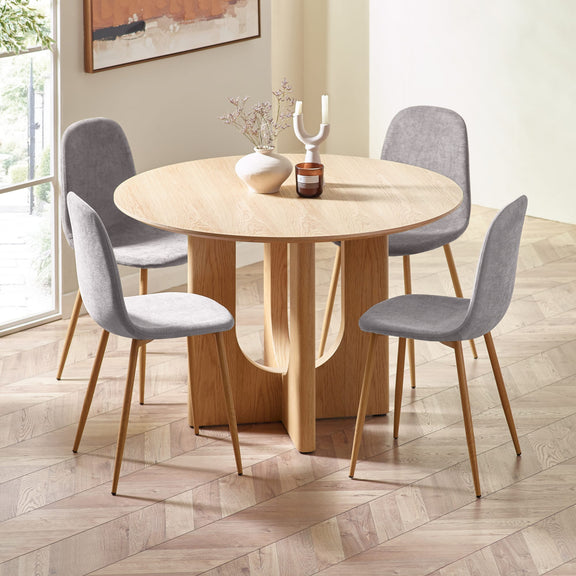 Round wooden dining table with four gray chairs in a well-lit room.