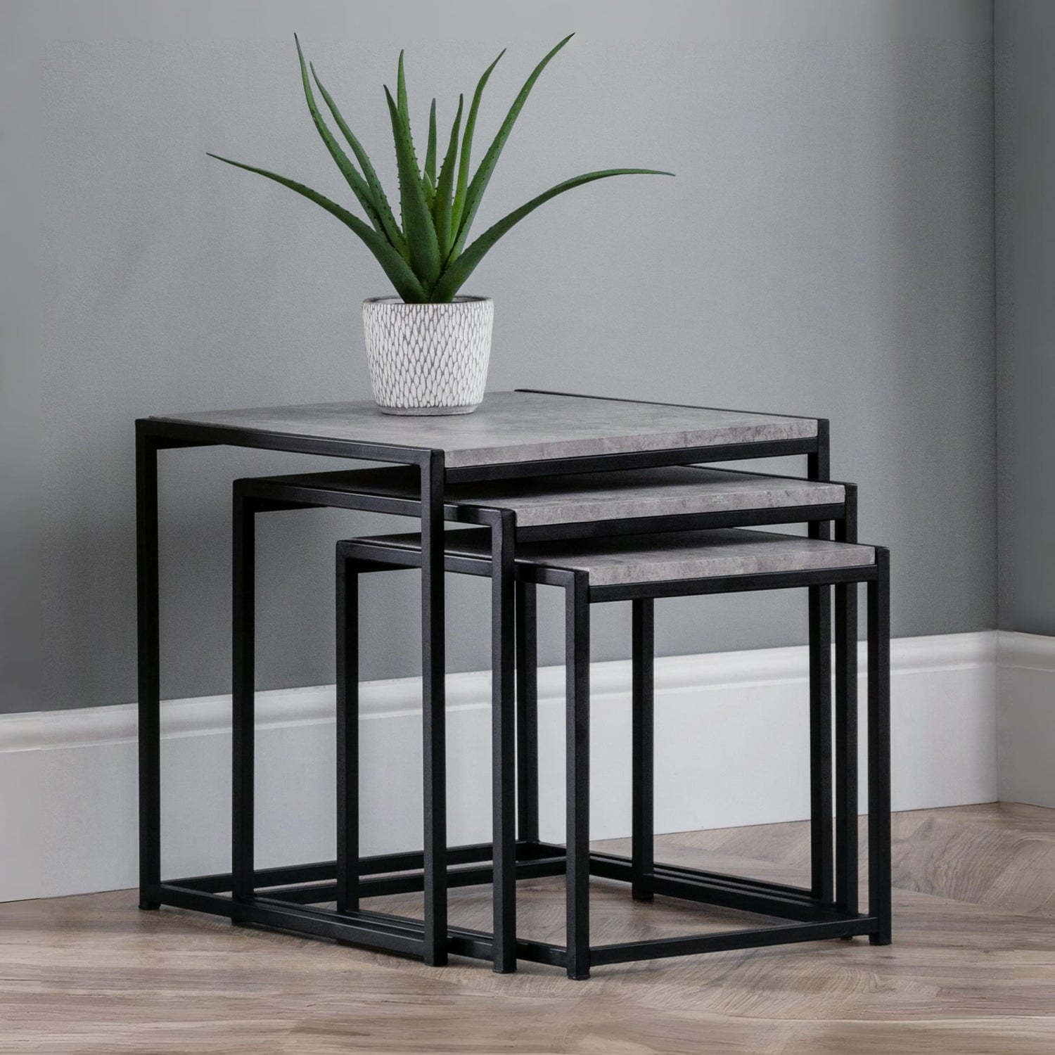 Set of three nesting tables with a plant on top against a gray wall.