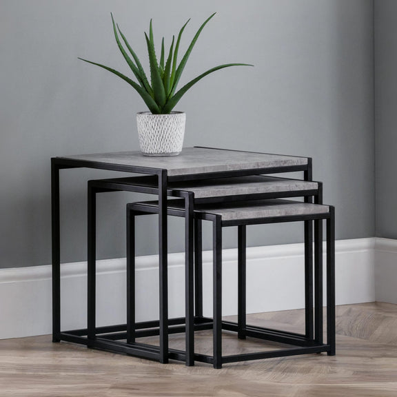 Set of three nesting tables with a plant on top against a gray wall.