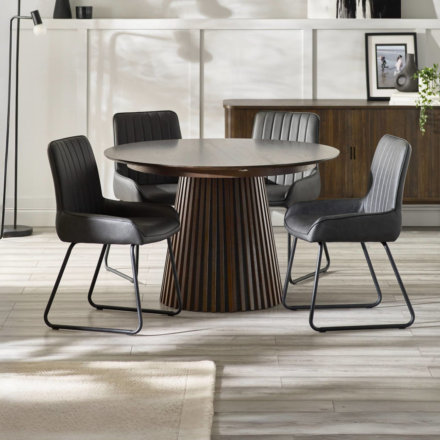 Round wooden dining table with four black chairs in a modern room.
