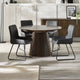 Round wooden dining table with four black chairs in a modern room.