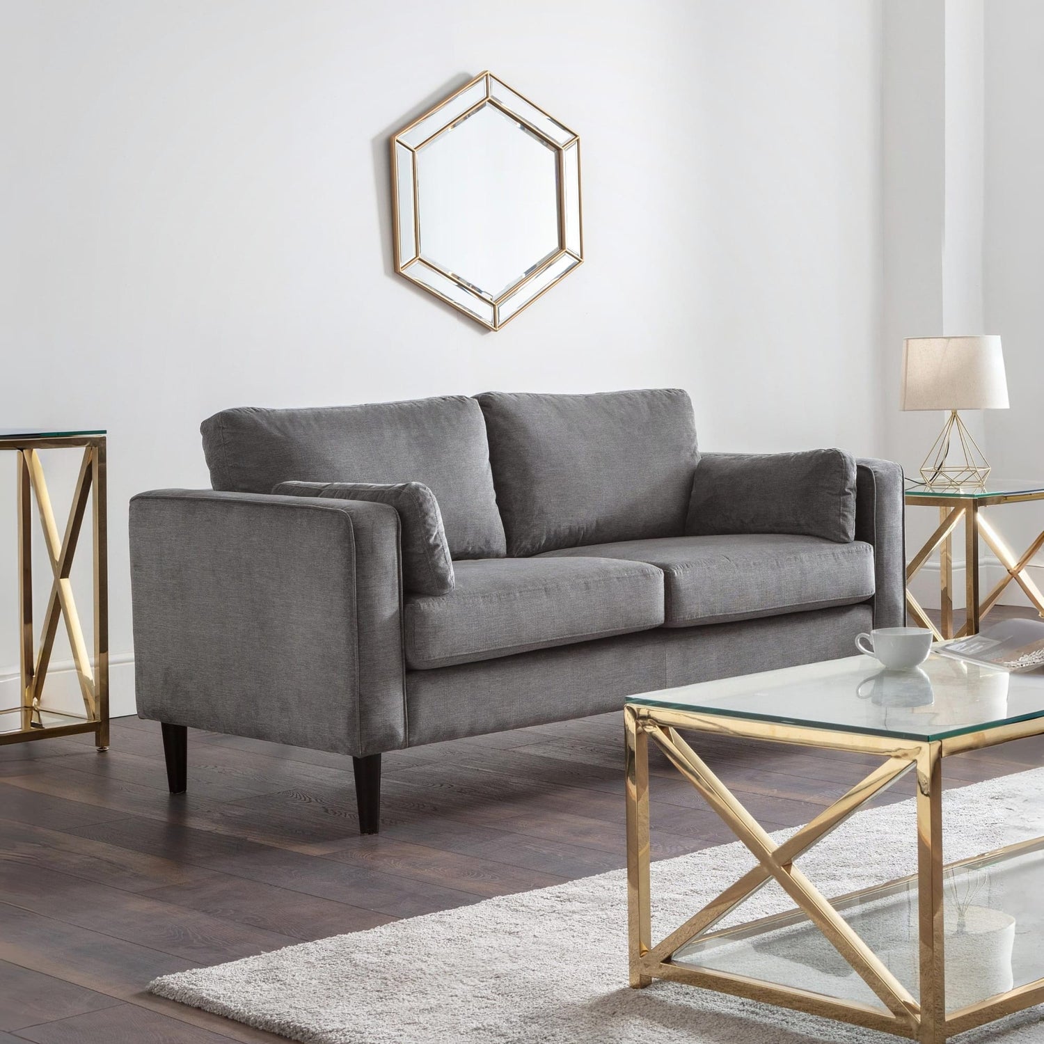 Gray sofa in a modern living room with gold accents and a hexagonal mirror.