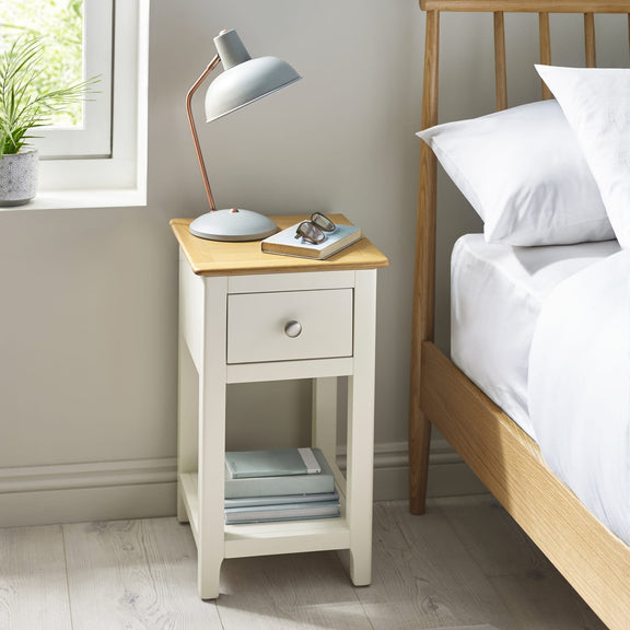 White wooden bedside table with oak top, single drawer and lower shelf beside bed