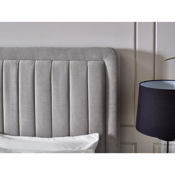 Gray upholstered headboard with a black lamp against a white wall
