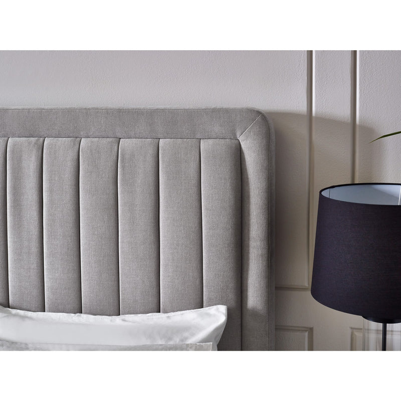 Gray upholstered headboard with a black lamp against a white wall