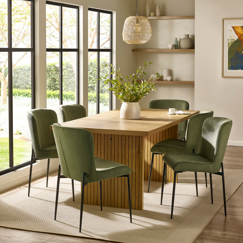 Dining room with wooden table and green chairs near large windows.