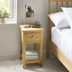 Wooden bedside table with lamp and books next to a bed in a bedroom.