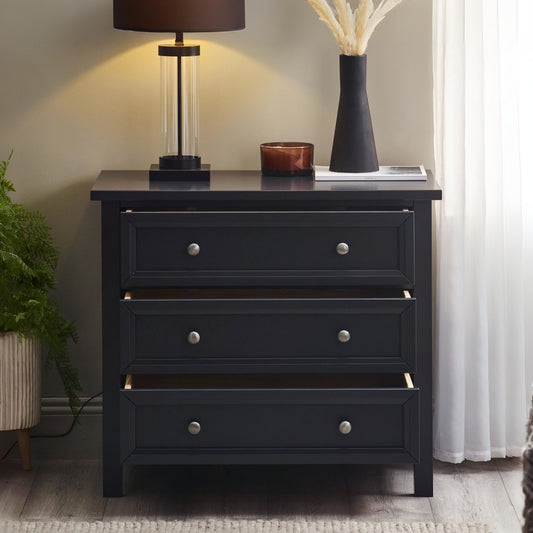 Black dresser with three drawers in a room setting with a lamp and decor items on top.