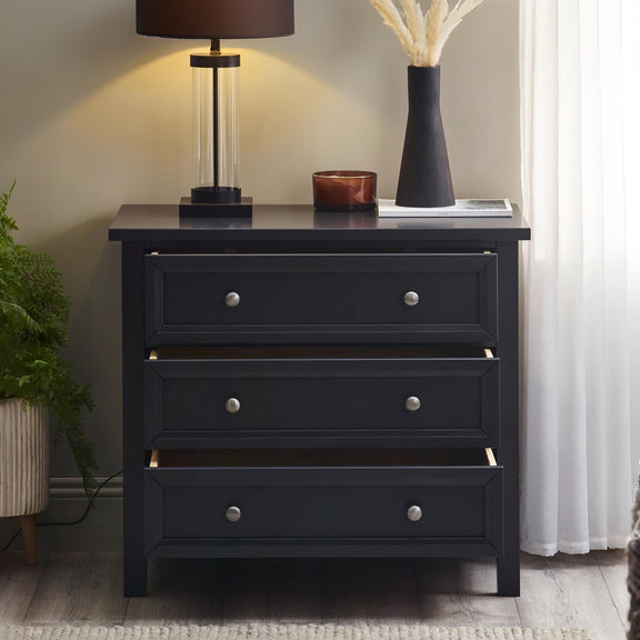 Black dresser with three drawers in a room setting with a lamp and decor items on top.