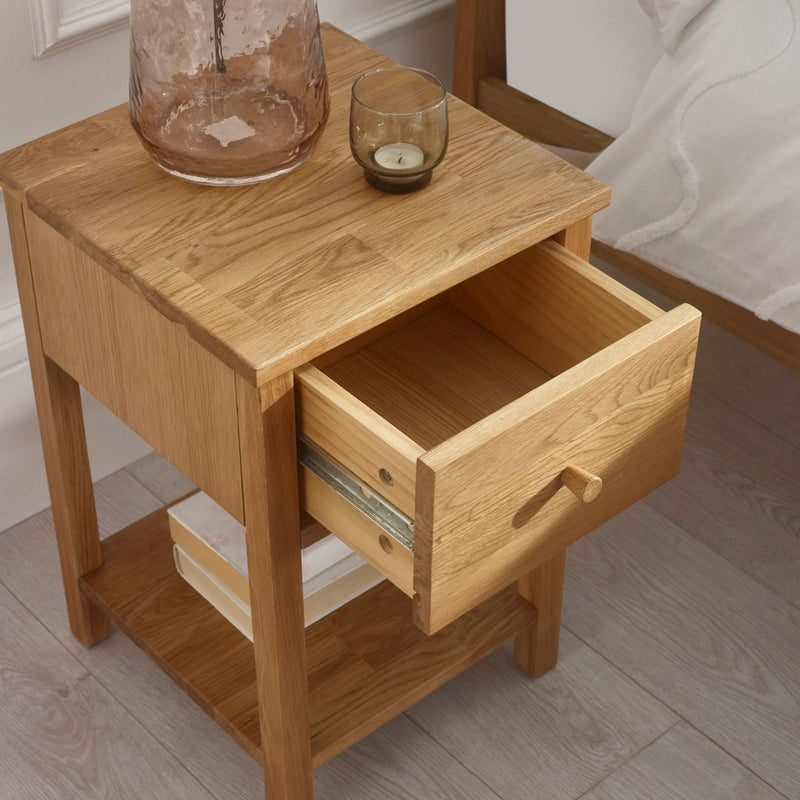 Wooden nightstand with open drawer, glass jar, and candle on a wooden floor.