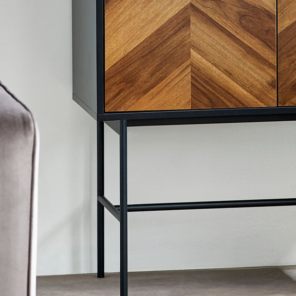 Cabinet with wooden chevron pattern doors and black metal frame against a white wall.
