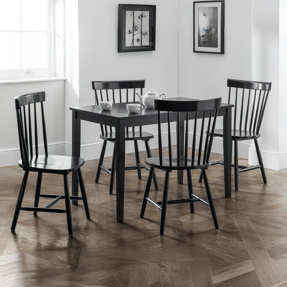 Black dining table with four chairs in a room with framed pictures on the wall.